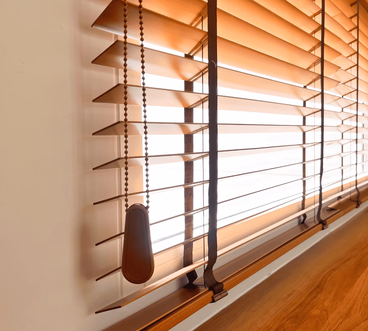 Brown venetian blinds with a beaded pull cord and weighted handle for domestic and commercial window styling.
