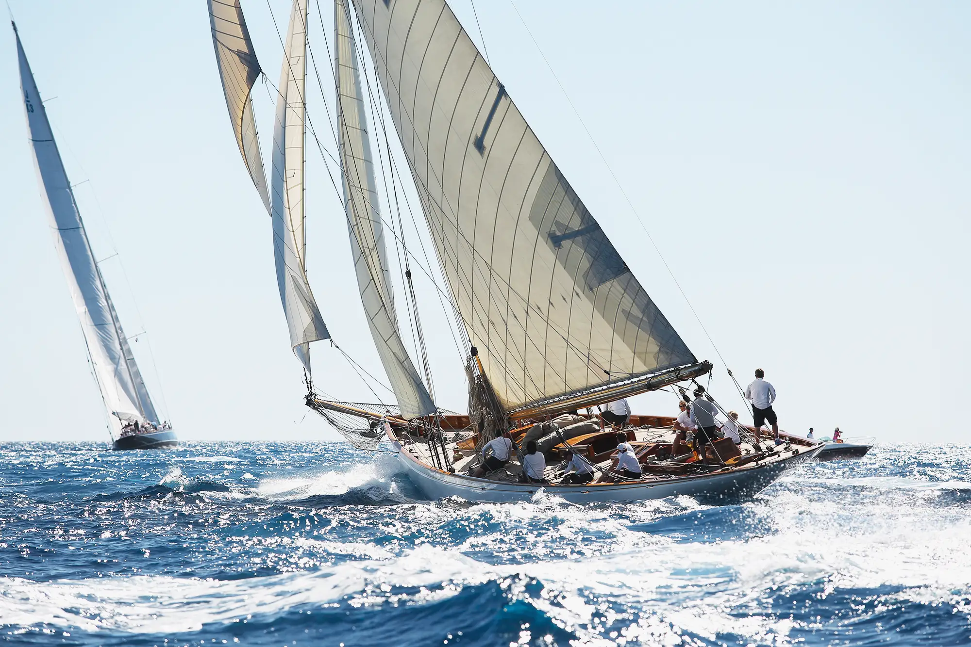 Classic sailing yacht under full sail in open water with crew on deck, traditional wooden gaff-rigged vessel racing