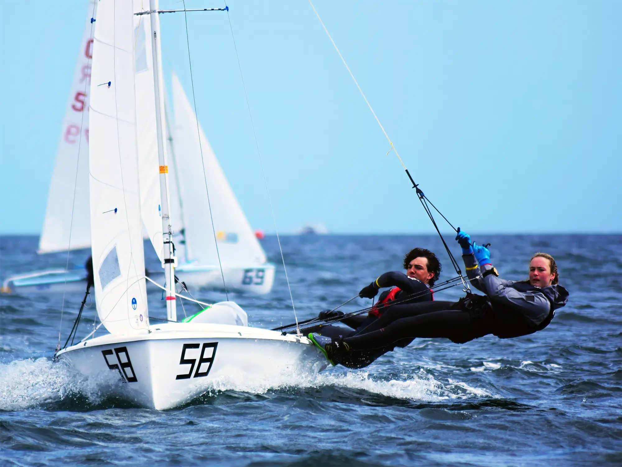 Two-person racing dinghy crew hiking out on starboard tack with sheets under load in competitive conditions