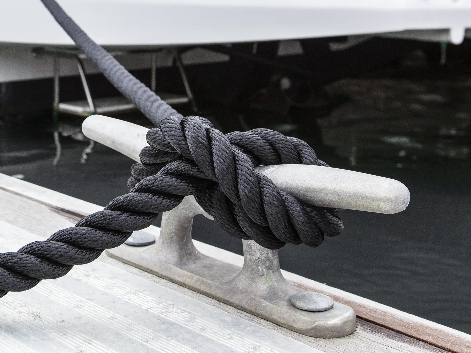 Black 3-Strand polyester rope tied in a cleat hitch on a stainless mooring cleat alongside a wooden dock