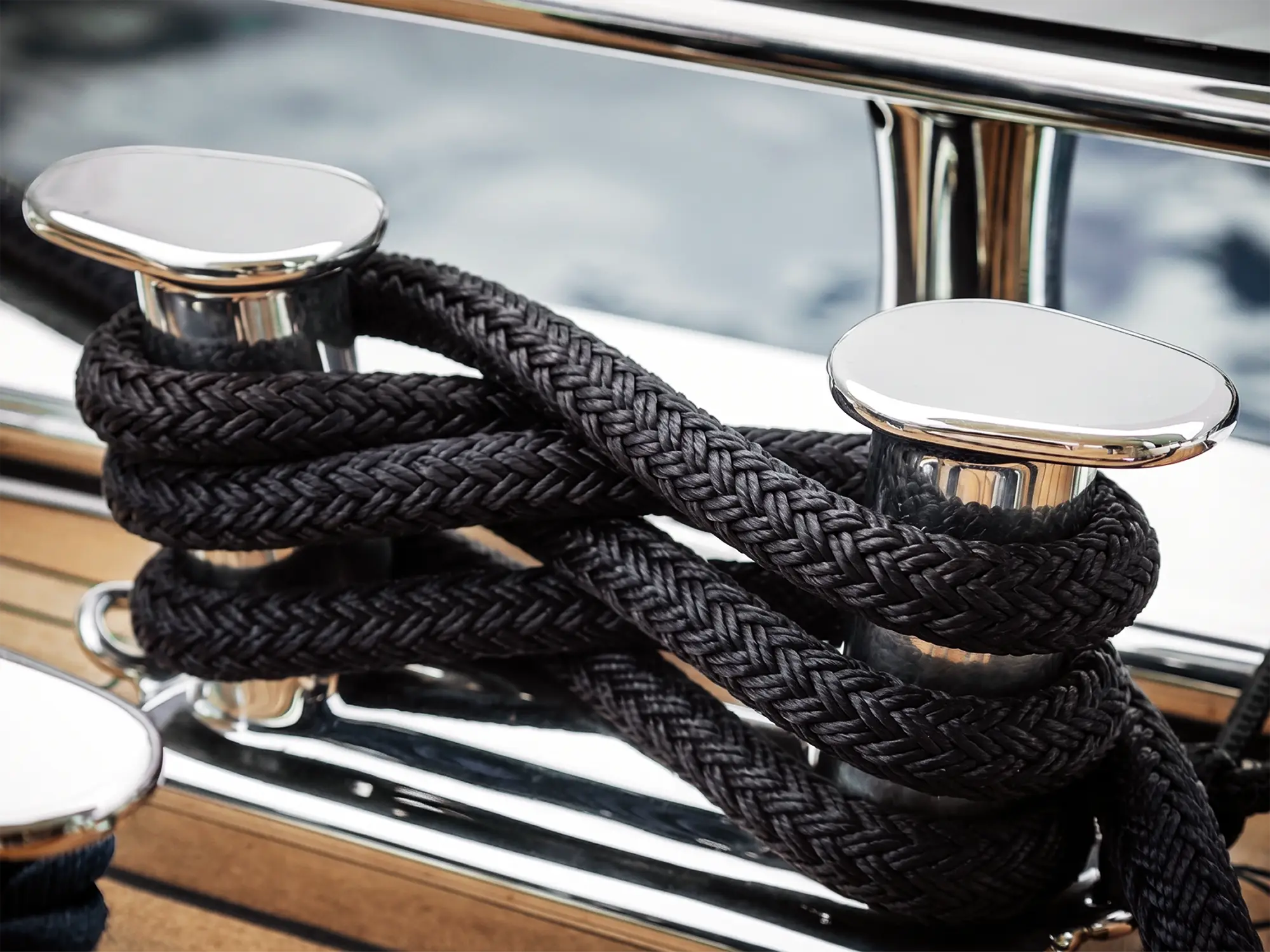 Large diameter black Dyneema® dockline coiled on polished stainless steel cleats on a superyacht teak deck