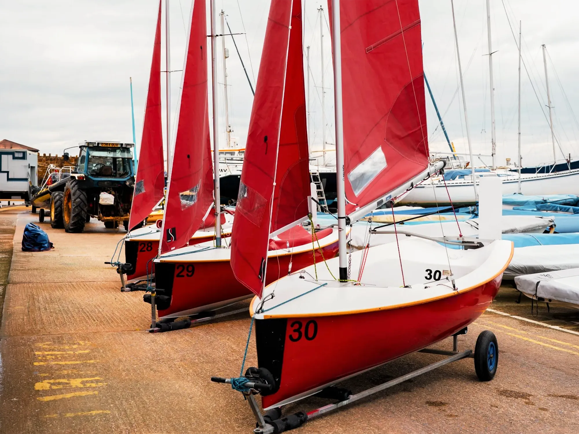 Three Mirror dinghies with red sails on trolleys at a sailing club, representing club dinghy racing