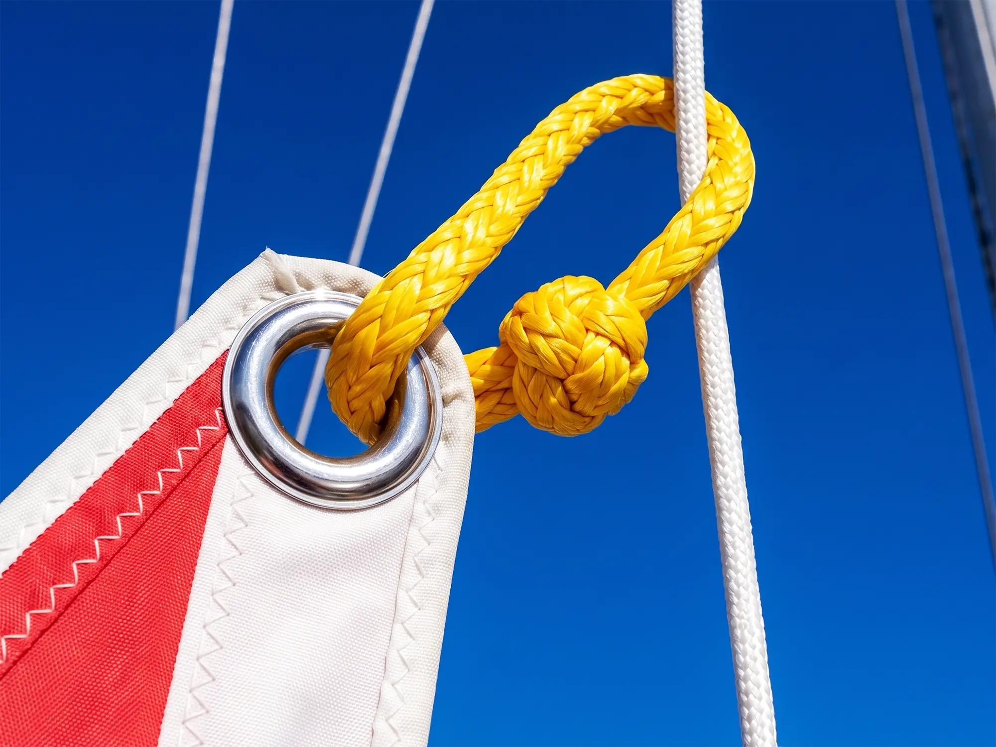 Yellow DC12 Dyneema® soft shackle connecting a sail clew to a stainless steel ring on a racing yacht