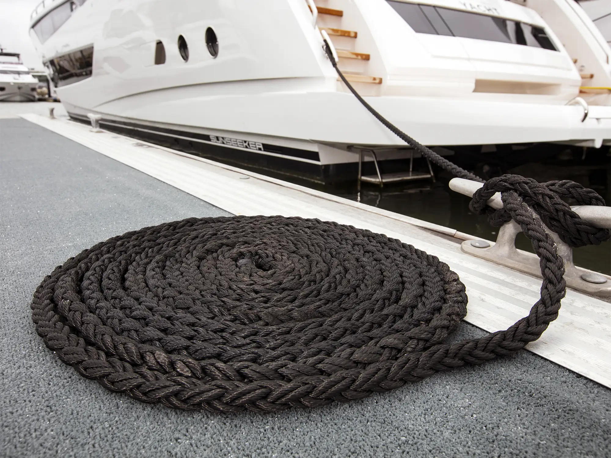 Coiled black 8-strand Anchorbraid on marina pontoon with motor yacht moored alongside